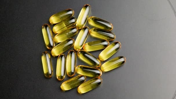 Group of golden transparent pills with liquid medicine rotating on black surface — Vídeos de Stock