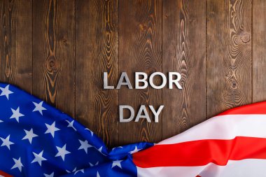 words labor day laid with silver metal letters on wooden surface with crumpled USA flag on bottom side