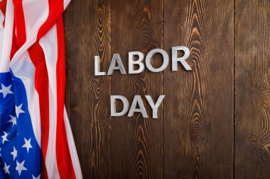 Tahta yüzeyde gümüş metal harflerle, sol tarafında buruşuk Amerikan bayrağıyla...