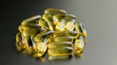 group of golden transparent pills with liquid medicine rotating on black surface