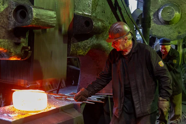 Blacksmith worker forging large piece of hot steel in old factory — Stock Fotó