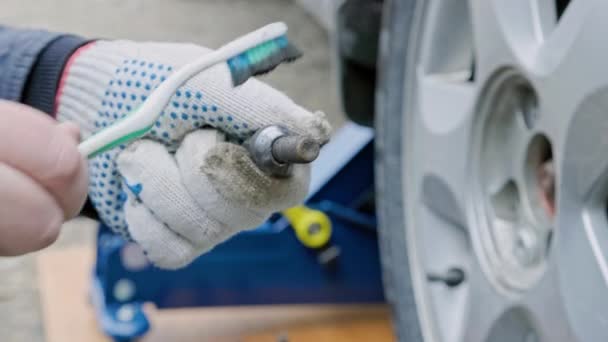 Hands of mechanic cleaning car wheel bolt with old tooth brush — Video Stock