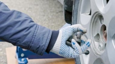 hands of mechanic unscrewing car wheel bolts and holding them