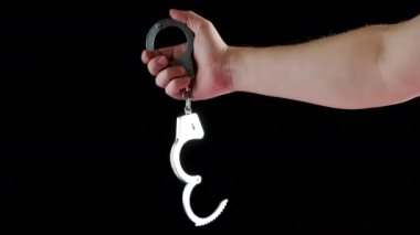 bare caucasian hand holding opened silver steel handcuffs on black background