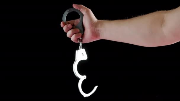 Bare caucasian hand holding opened silver steel handcuffs on black background — Stockvideo