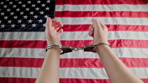 Caucasian hands shackled in silver handcuffs against the USA flag — Stock video
