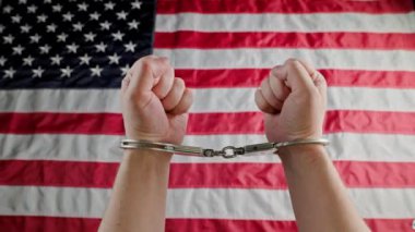 caucasian hands shackled in silver handcuffs against the USA flag