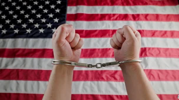 Caucasian hands shackled in silver handcuffs against the USA flag — Stockvideo