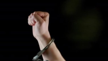 rised fist of caucasian hand shakled in siver handcuffs against black background