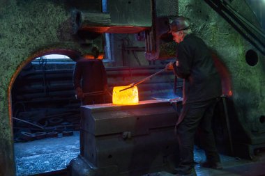 blacksmith worker taking large piece of hot steel with big forceps in old factory