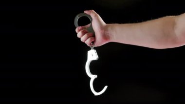 bare caucasian hand holding opened silver steel handcuffs on black background