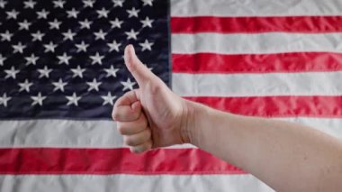 thumbs up gesture made with caucasian hand in front of blurry US flag