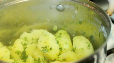 caucasian hand opens lid of casserole with steamy boiled potatoes with dill