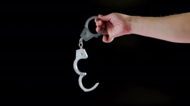 bare caucasian hand holding opened silver steel handcuffs on black background