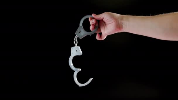 Bare caucasian hand holding opened silver steel handcuffs on black background — Vídeo de stock