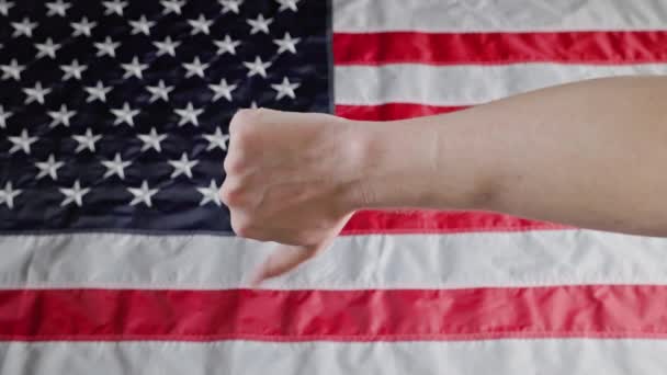 Thumbs up and thumbs down gestures made with caucasian hand in front of blurry US flag — Wideo stockowe