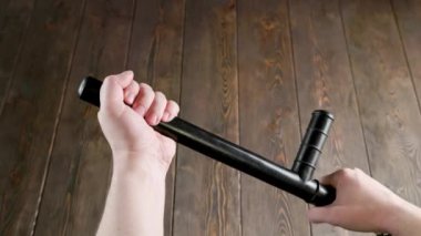 caucasian hands holding black rubber police tonfa baton over wooden surface
