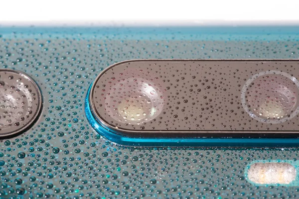 Lente de la cámara del teléfono perla verde aurora cubierta con pequeñas gotas de agua - primer plano con enfoque selectivo y desenfoque — Foto de Stock