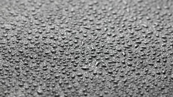 Spinning closeup background of black hydrophobic fabric covered with water drops — Video