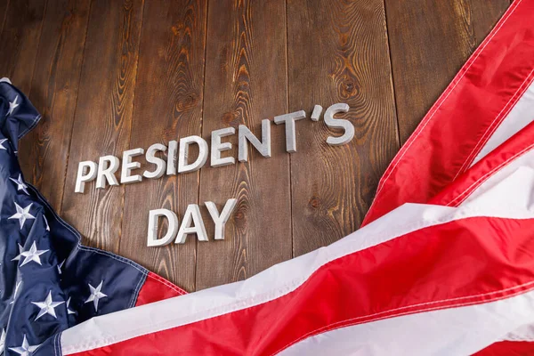 words presitdents day laid with silver letters on wooden surface near US flag