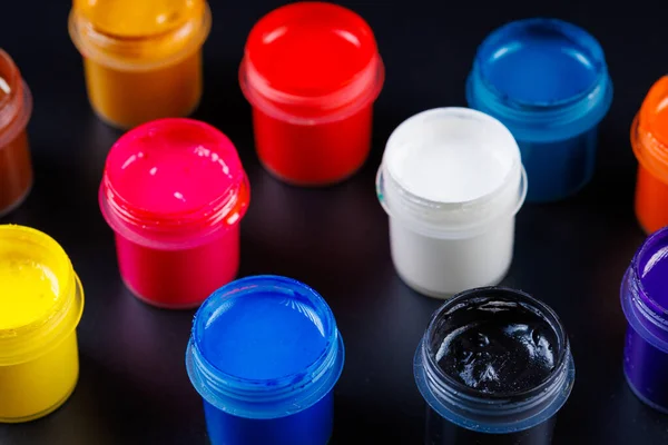 Full-frame close-up view d of opened small gouache paint jars on black surface — Stockfoto