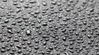 spinning closeup background of black hydrophobic fabric covered with water drops