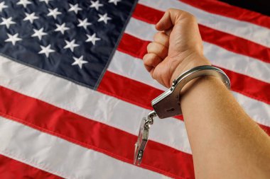 caucasian hand cuffed with silver metal handcuffs over US flag background