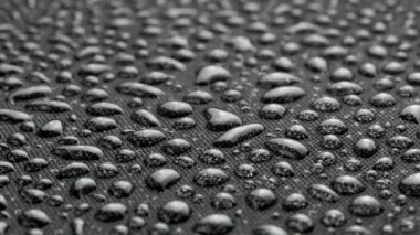 spinning closeup background of black hydrophobic fabric covered with water drops