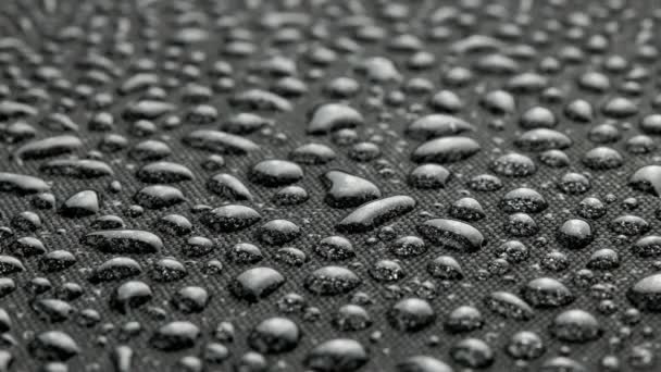 Spinning closeup background of black hydrophobic fabric covered with water drops — Video