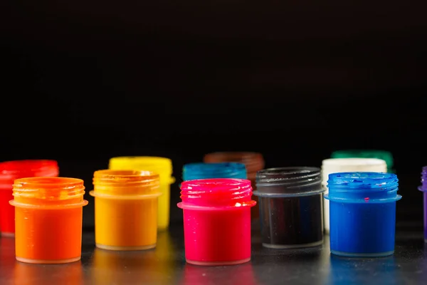 Close-up background of opened small gouache paint jars on black surface — Stockfoto