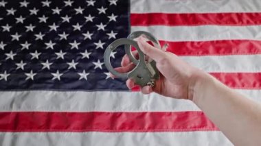 caucasian hand holding silver metal handcuffs over blurry US flag