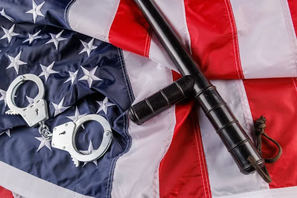 Серебряные металлические наручники и полицейская дубинка над флагом США на плоской поверхности — стоковое фото