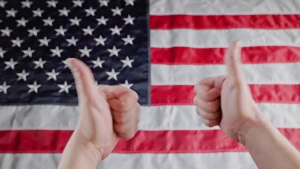 Великий палець вгору жест, зроблений двома кавказькими руками перед розмитим прапором США — стокове відео