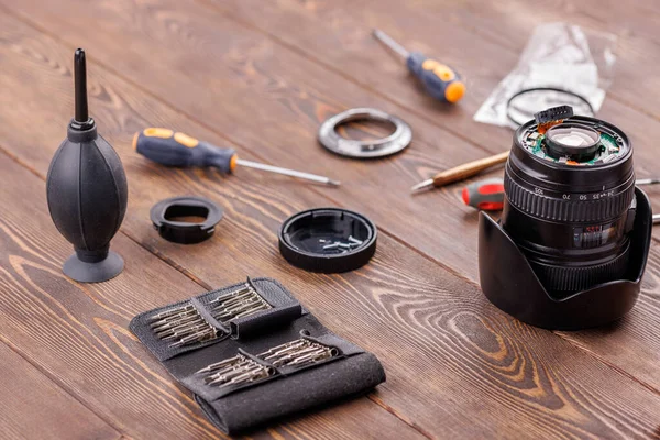 Half-disassembled camera zoom lens on wooden table surrounded with tools — Fotografia de Stock