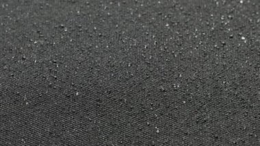 spinning closeup background of black hydrophobic fabric covered with water drops