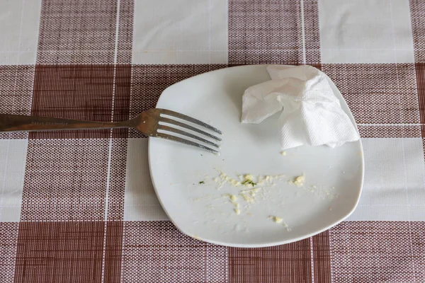 Empty white dish with leftovers of eaten food, crumpled table-napkin and steel fork — Stok fotoğraf