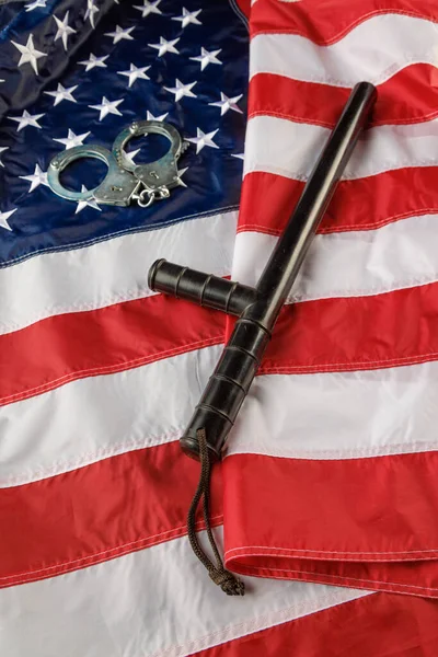 Silver metal handcuffs and police nightstick over US flag on flat surface — Foto de Stock