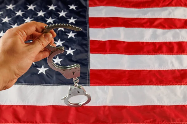 caucasian hand holding silver metal handcuffs over US flag background
