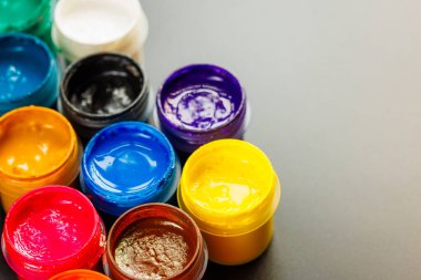 close-up background of opened small gouache paint jars on black surface