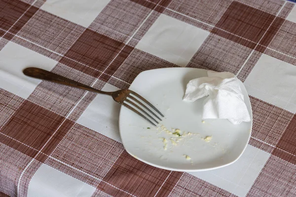 Empty white dish with leftovers of eaten food, crumpled table-napkin and steel fork — Stok fotoğraf
