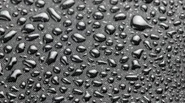 spinning closeup background of black hydrophobic fabric covered with water drops