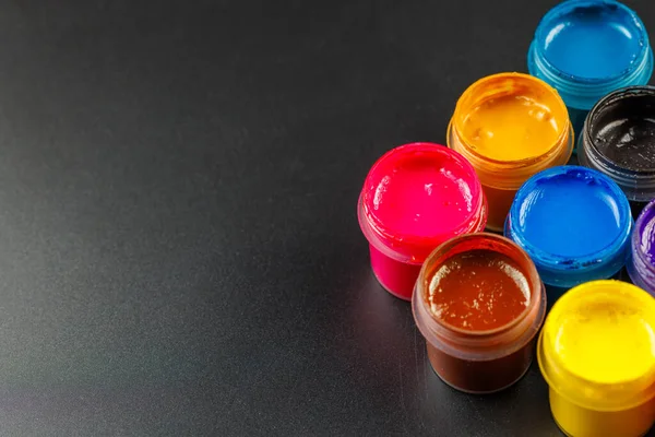 Close-up background of opened small gouache paint jars on black surface — Stockfoto