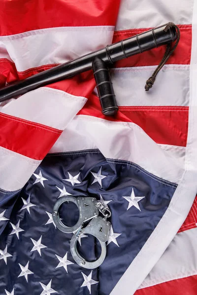 Серебряные металлические наручники и полицейская дубинка над флагом США на плоской поверхности — стоковое фото