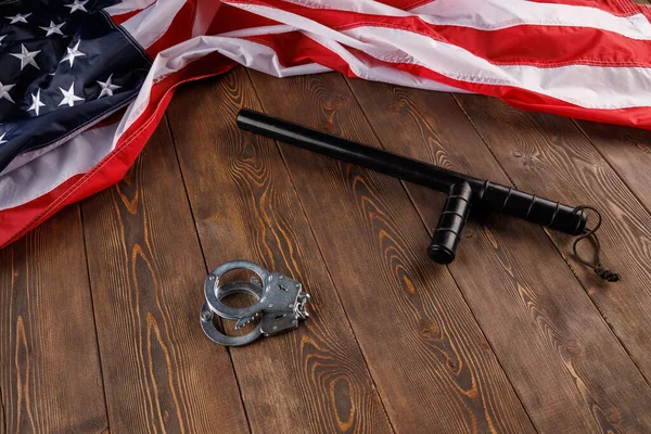 Ασημένιες μεταλλικές χειροπέδες και αστυνομικό κλομπ κοντά στη σημαία των ΗΠΑ σε ξύλινη επιφάνεια — Φωτογραφία Αρχείου