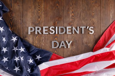 words presitdents day laid with silver letters on wooden surface near US flag