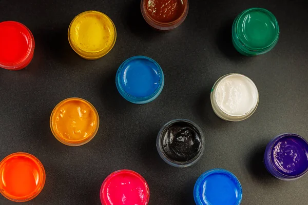 Full-frame close-up view d of opened small gouache paint jars on black surface — Stockfoto