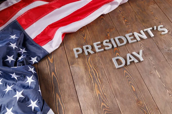 words presitdents day laid with silver letters on wooden surface near US flag