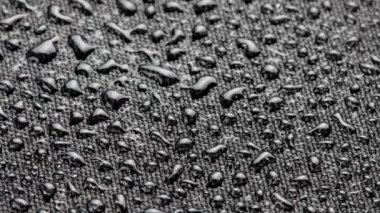 spinning closeup background of black hydrophobic fabric covered with water drops