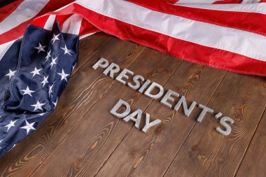 words presitdents day laid with silver letters on wooden surface near US flag