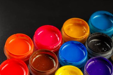close-up background of opened small gouache paint jars on black surface